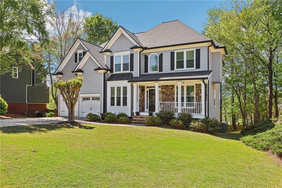 View of front facade featuring an attached garage, driveway, covered porch, roof with shingles, and a front yard