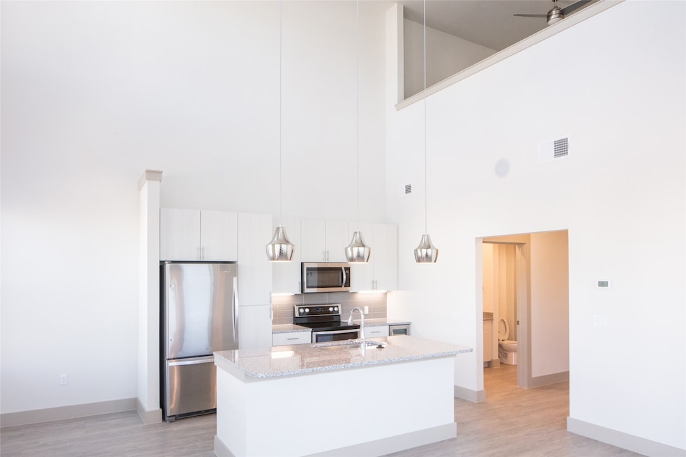 Kitchen with pendant lighting, ceiling fan, a towering ceiling, white cabinetry, and stainless steel appliances