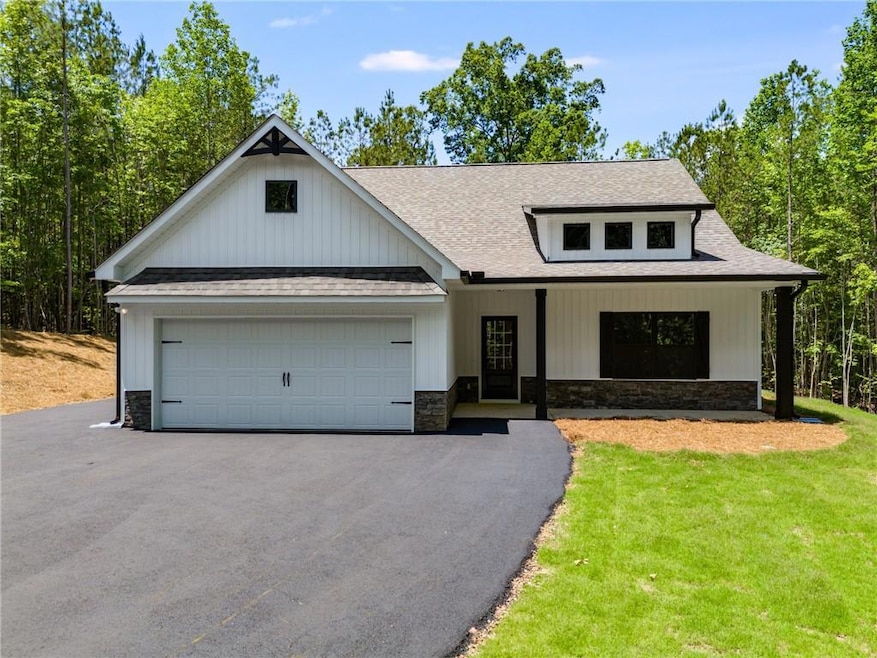View of front of house with roof with shingles, asphalt driveway, an attached garage, and stone siding