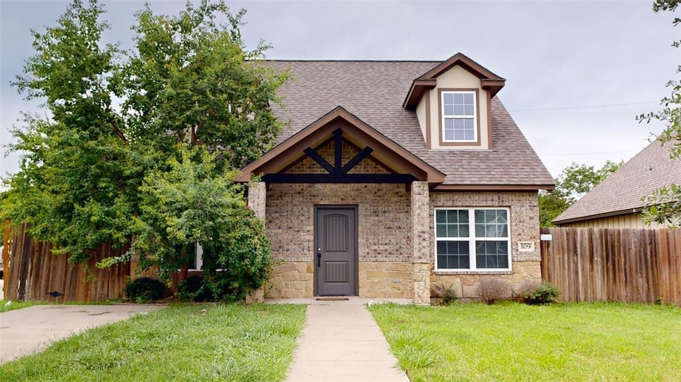 View of front of house featuring a shingled roof, stone siding, and brick siding