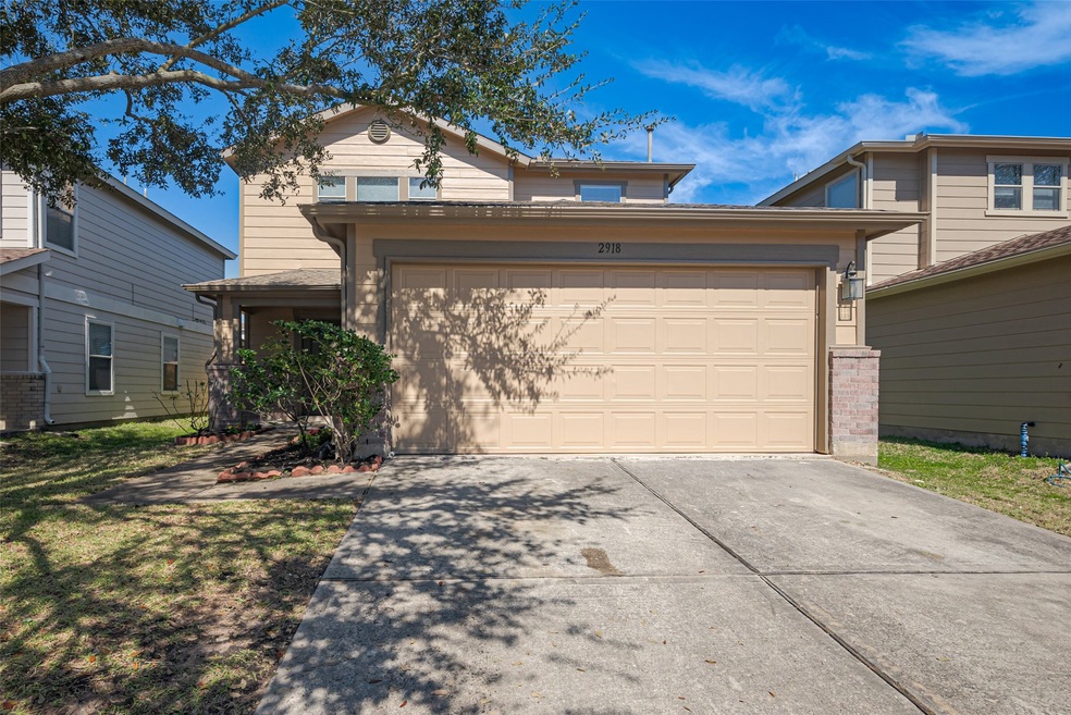 This is a two-story home with a beige exterior and a two-car garage. It features a concrete driveway, a front yard with neat landscaping.