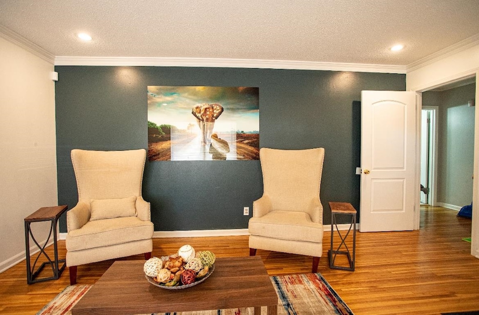 Living area with a textured ceiling, wood finished floors, ornamental molding, baseboards, and recessed lighting