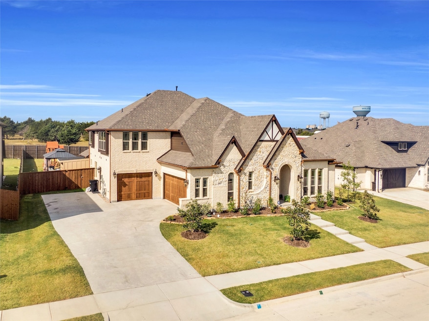 View of front facade featuring driveway, brick siding, an attached garage, and stone siding