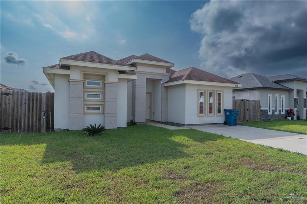 View of front facade featuring a shingled roof, fence, stucco siding, and a front yard