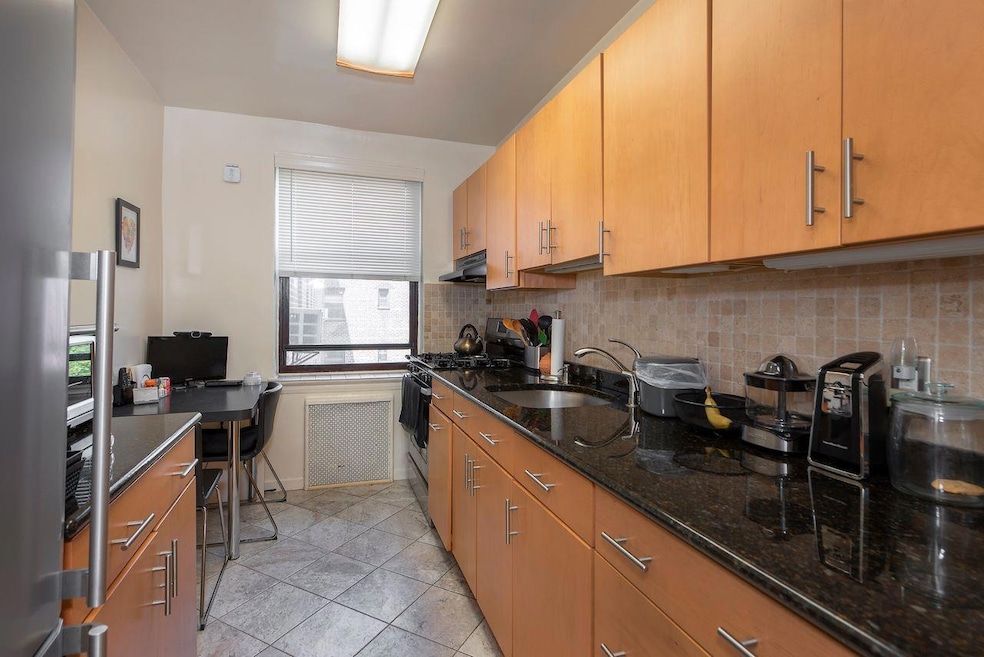 Kitchen with decorative backsplash, freestanding refrigerator, dark stone countertops, gas stove, and an eat-in area