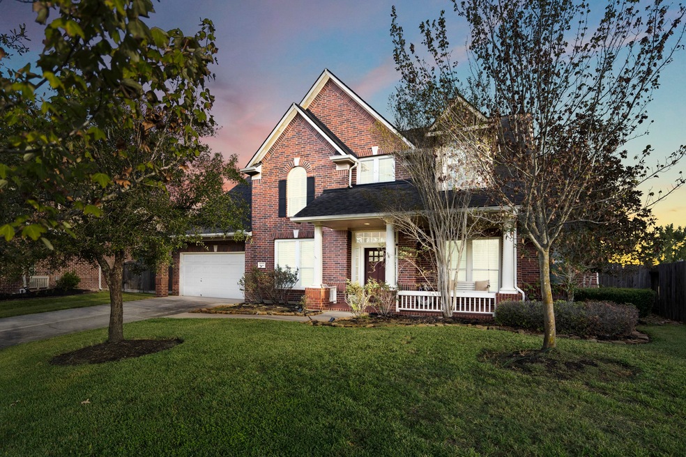 This is a two-story brick home with a prominent gable roof,  and a welcoming front porch. The property features a well-manicured lawn and mature trees, offering a serene suburban setting.