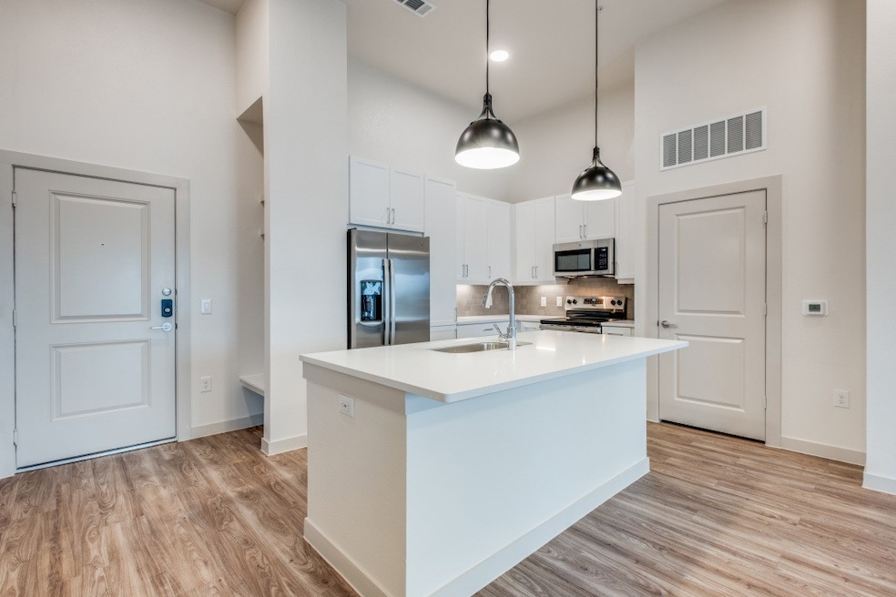 Kitchen with appliances with stainless steel finishes, a high ceiling, a center island with sink, white cabinetry, and light wood finished floors