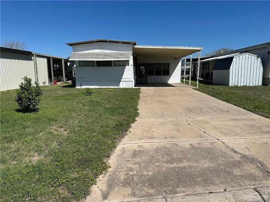Manufactured / mobile home featuring an outbuilding, an attached carport, a front lawn, and a shed