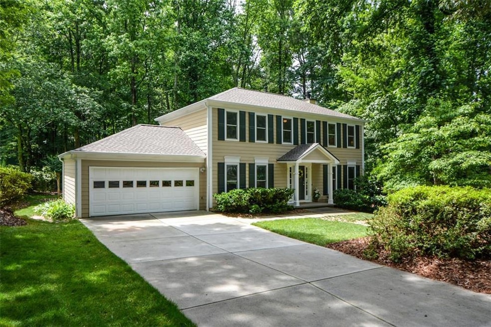Colonial house featuring concrete driveway, a garage, roof with shingles, and a front lawn