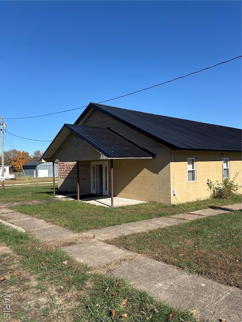 View of property exterior with concrete block siding, a yard, and a metal roof