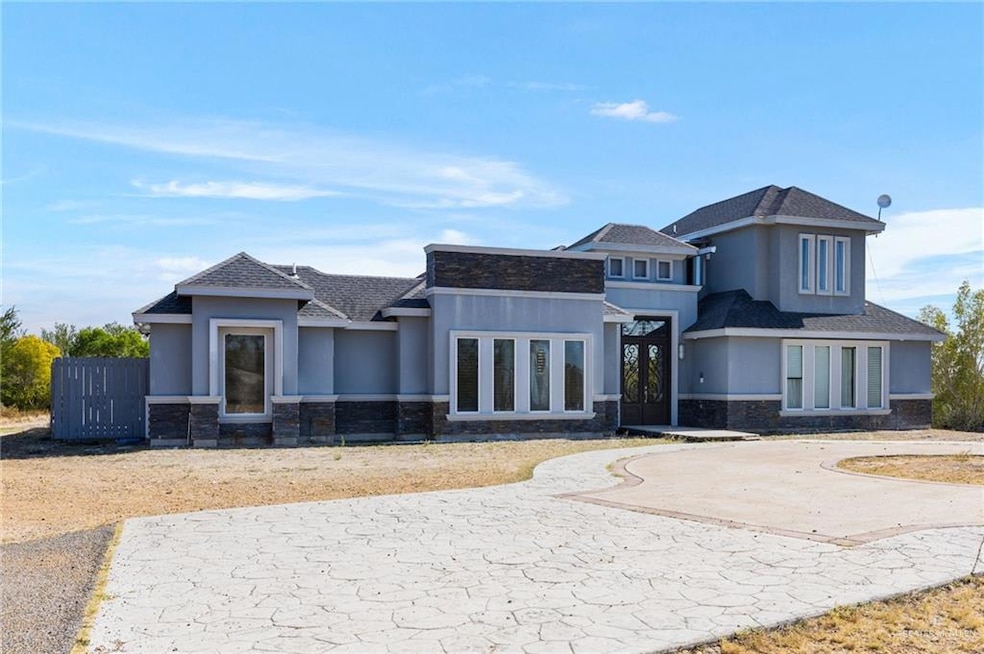 Prairie-style home with stone siding, a shingled roof, stucco siding, and curved driveway