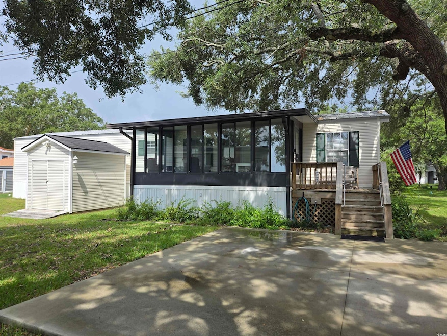 View of front of house featuring a sunroom, a storage shed, a front yard, and a patio
