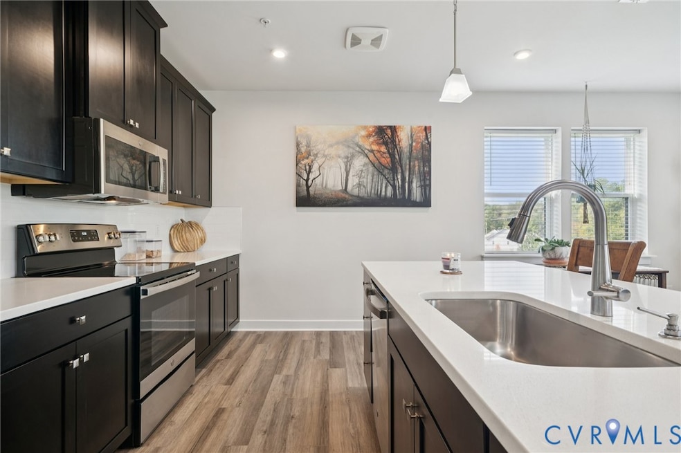 Kitchen with appliances with stainless steel finishes, light wood-style floors, hanging light fixtures, recessed lighting, and dark cabinetry