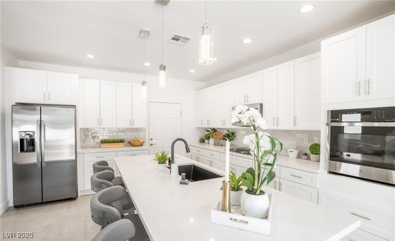Kitchen with stainless steel appliances, hanging light fixtures, a kitchen breakfast bar, white cabinets, and tasteful backsplash