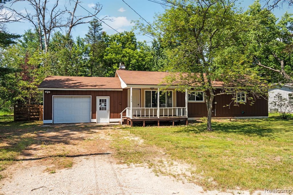 View of front of property with dirt driveway, covered porch, a garage, a front yard, and a shingled roof