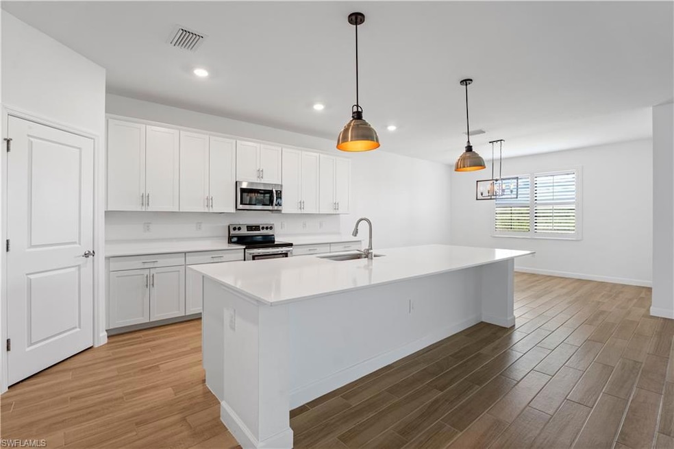 Kitchen featuring white cabinetry, pendant lighting, stainless steel appliances, a kitchen island with sink, and light wood finished floors