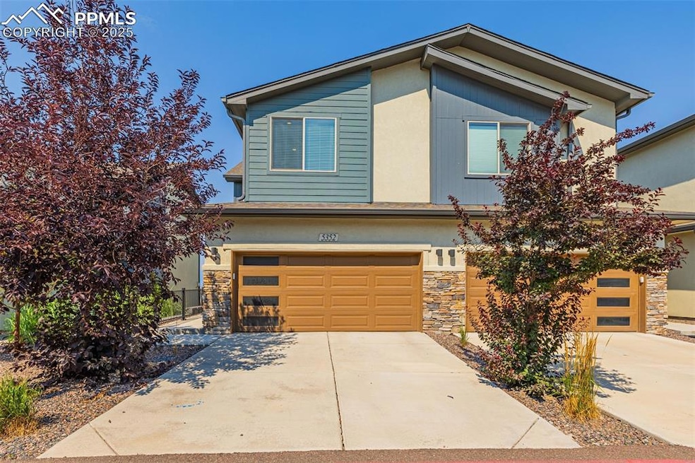 View of front facade featuring stone siding, driveway, and an attached garage