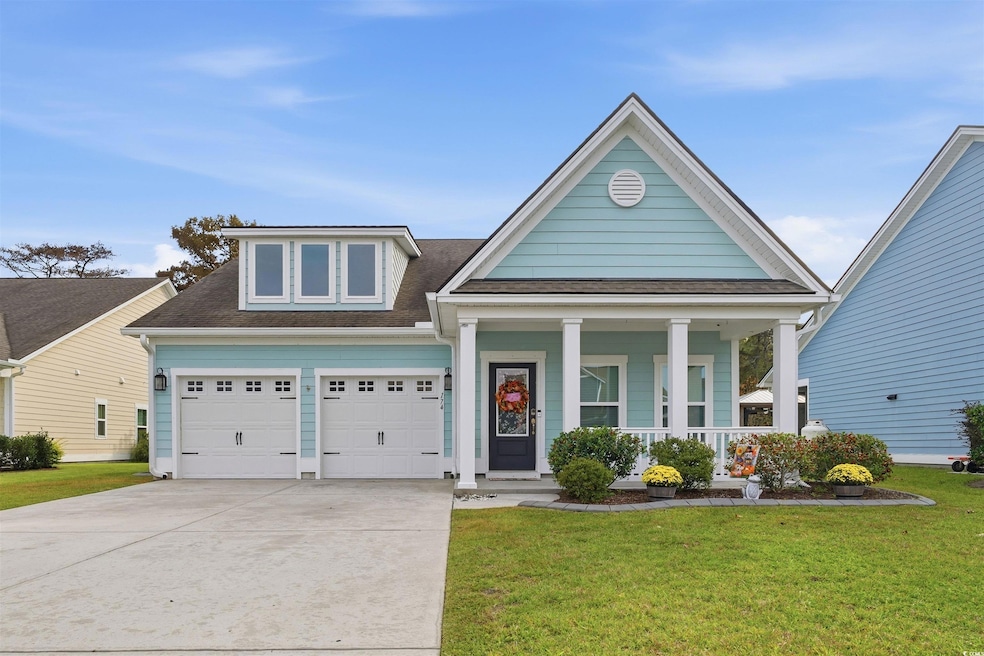 View of front of house with covered porch, a front yard, a shingled roof, and driveway