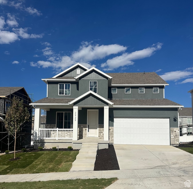 Craftsman-style home with covered porch, stone siding, driveway, and a front lawn