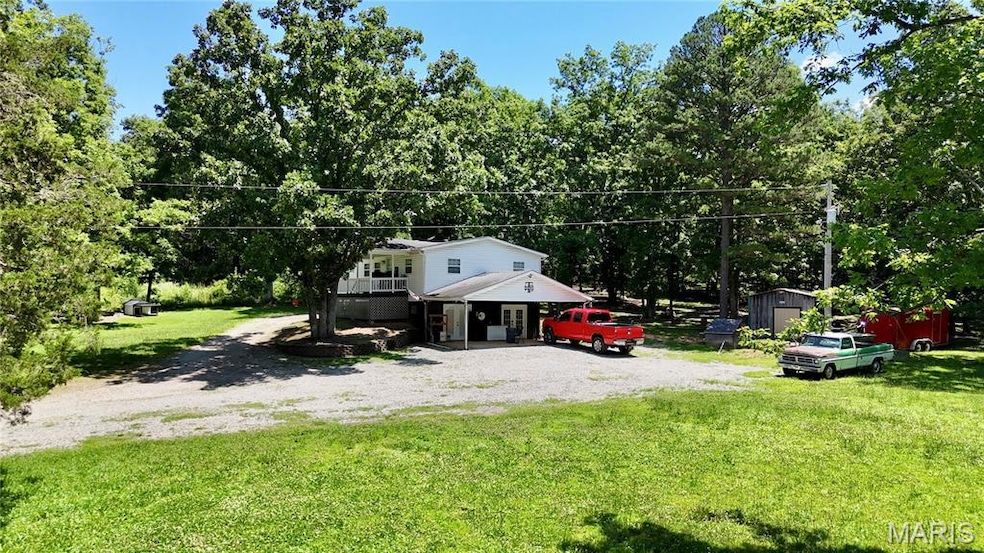 View of front of property with a front lawn, gravel driveway, view of scattered trees, and a shed