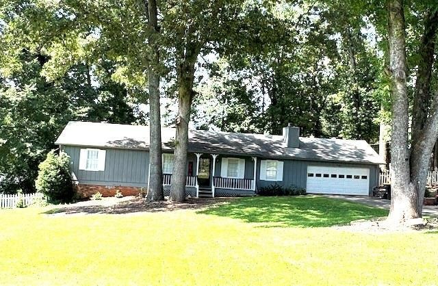 Ranch-style house with an attached garage, a porch, a chimney, and driveway
