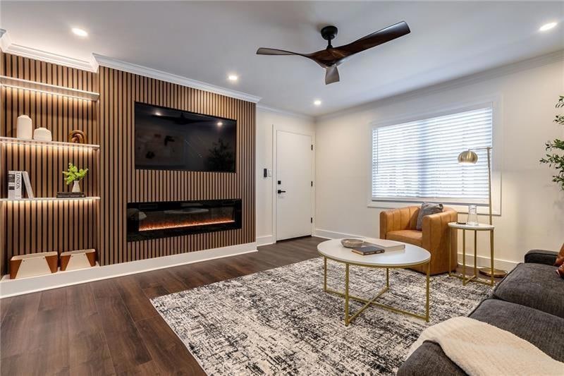 Living area featuring ceiling fan, ornamental molding, baseboards, wood finished floors, and a glass covered fireplace
