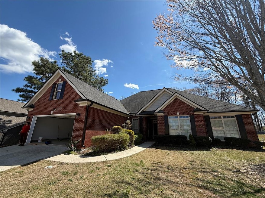 View of front of home featuring brick siding, driveway, a front lawn, and a shingled roof
