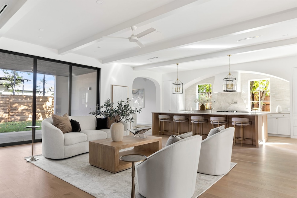Living room with light wood-style flooring, beam ceiling, arched walkways, and ceiling fan