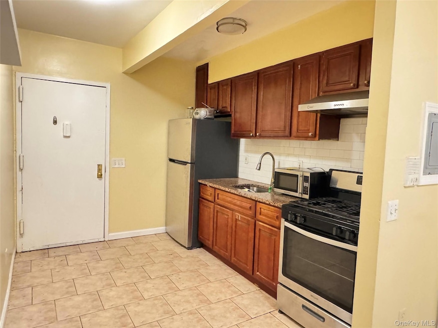 Kitchen featuring stainless steel appliances, decorative backsplash, dark stone countertops, and brown cabinetry