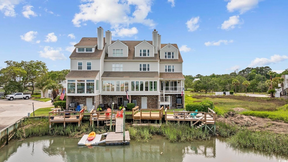 Rear view of house featuring a water view, a shingled roof, stone siding, and a chimney