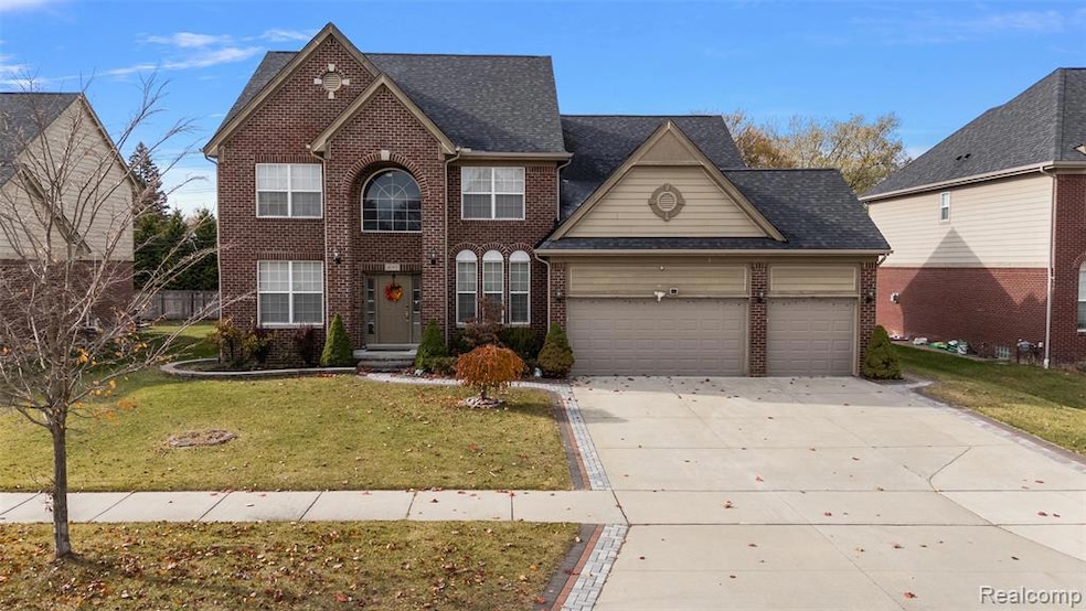 Traditional-style home featuring brick siding, a front yard, concrete driveway, an attached garage, and roof with shingles