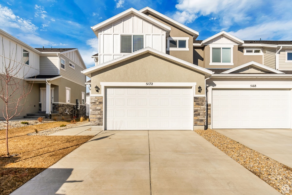View of front facade with stone siding, concrete driveway, board and batten siding, and stucco siding