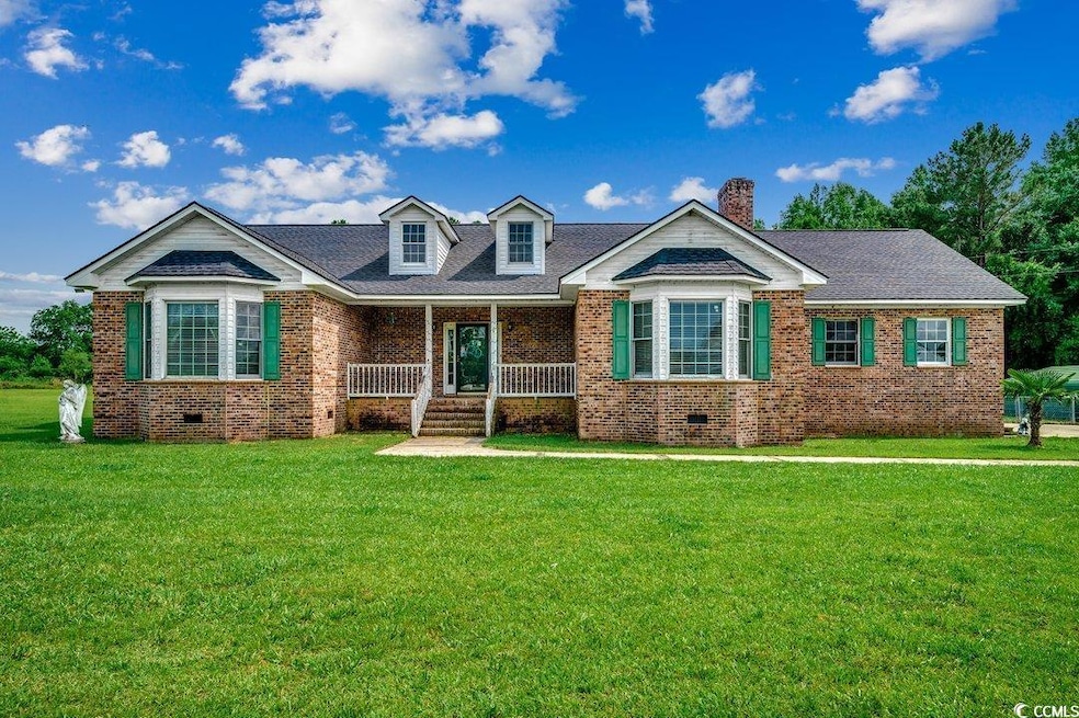 View of front of home featuring brick siding, a porch, a front lawn, and a chimney