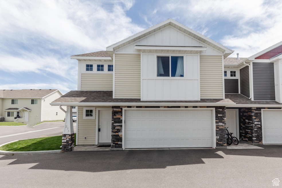 Townhome / multi-family property with board and batten siding, a garage, a shingled roof, asphalt driveway, and stone siding