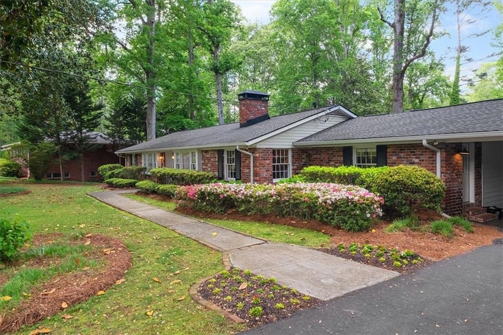 Ranch-style home with a chimney, brick siding, a front yard, and a shingled roof