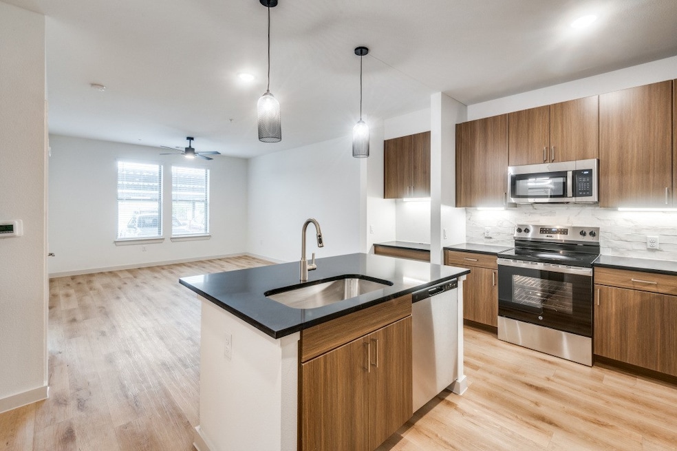 Kitchen with dark countertops, stainless steel appliances, brown cabinets, and light wood finished floors