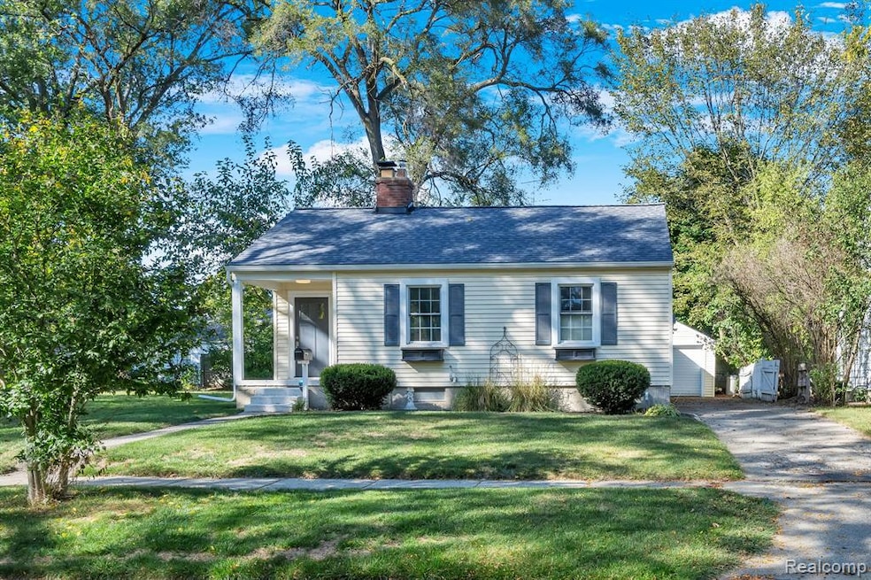 View of front of house featuring a front lawn, a chimney, an outdoor structure, a shingled roof, and driveway