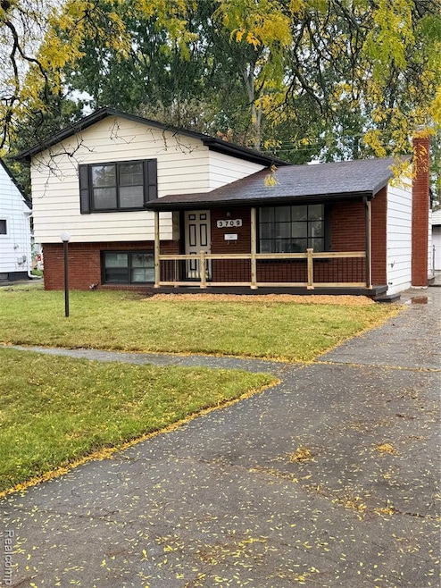Split level home featuring a porch, a front yard, brick siding, and a garage