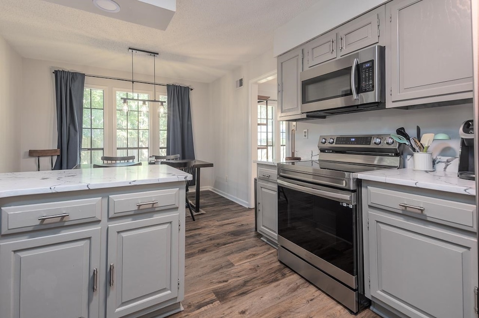 Kitchen featuring gray cabinets, stainless steel appliances, light stone counters, pendant lighting, and a textured ceiling