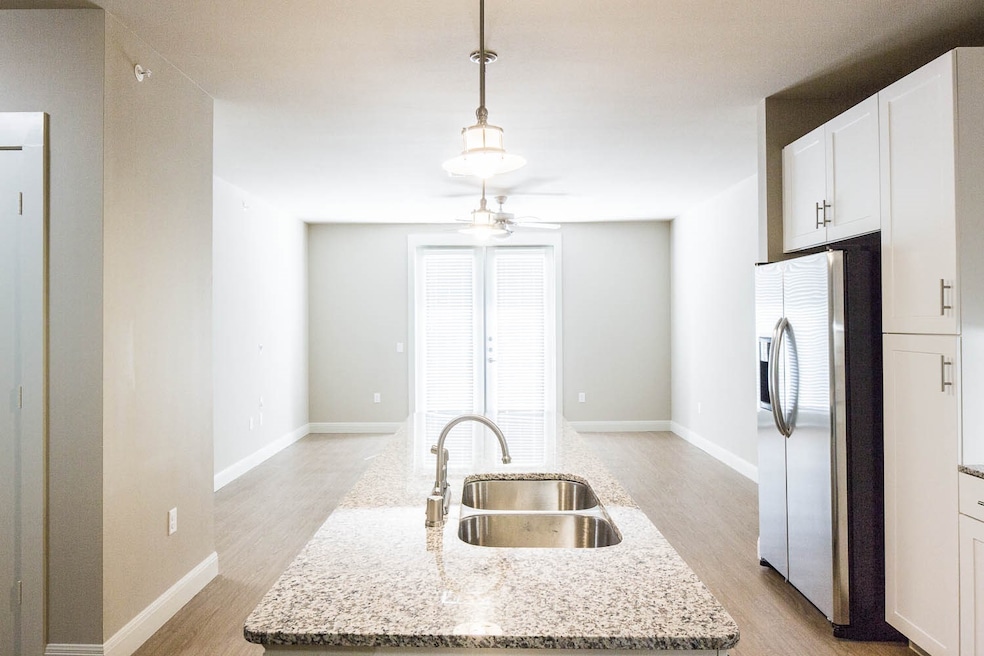 Kitchen featuring stainless steel fridge with ice dispenser, light wood-style flooring, decorative light fixtures, white cabinets, and light stone countertops