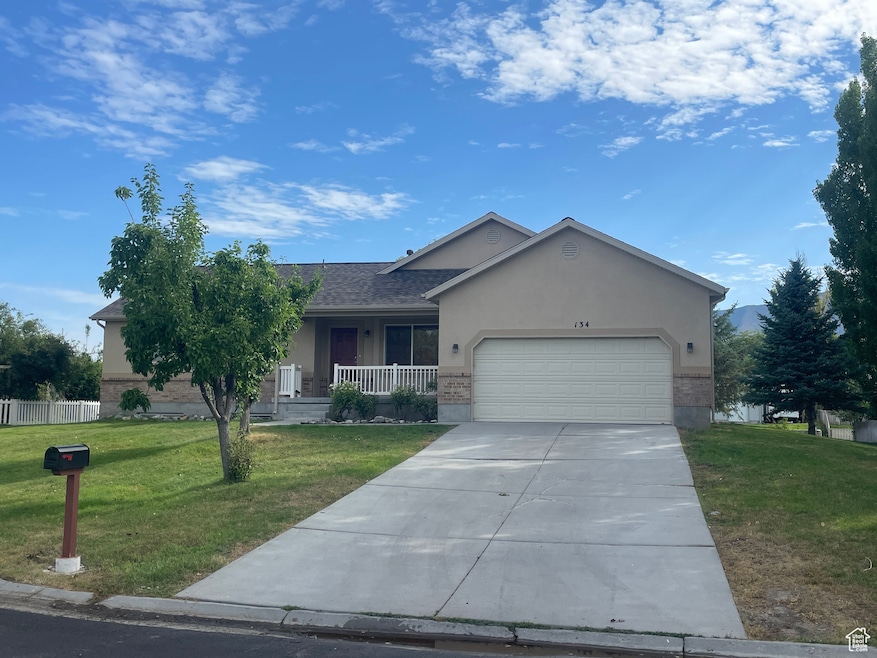 Single story home featuring covered porch, a front lawn, brick siding, concrete driveway, and stucco siding