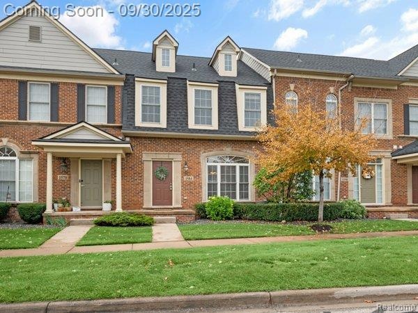View of front of home with a front yard, brick siding, and roof with shingles