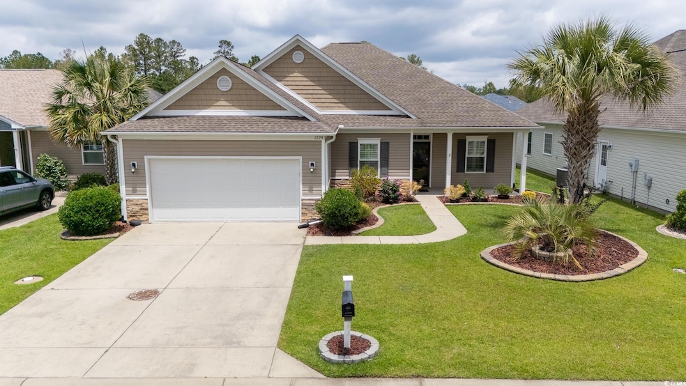 View of front of property with a front yard, concrete driveway, an attached garage, roof with shingles, and stone siding