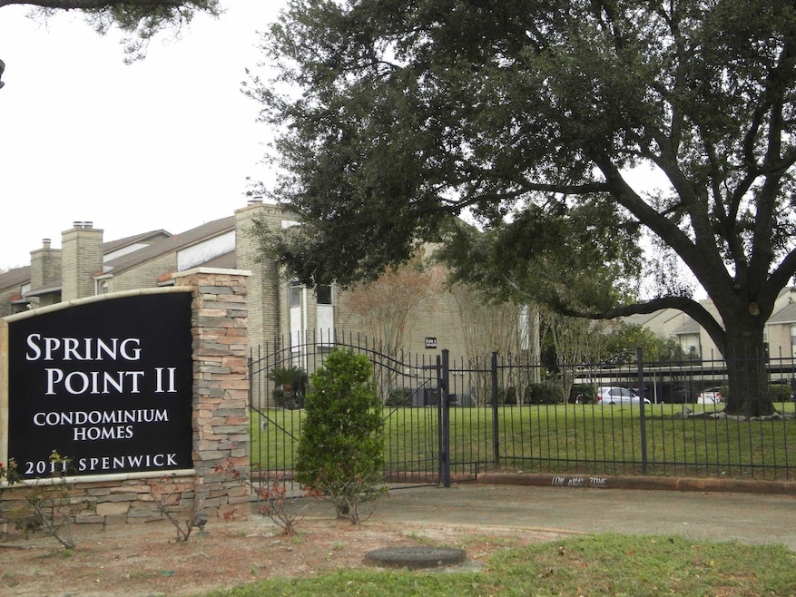 This photo shows the entrance to Spring Point II Condominium Homes, featuring a well-maintained area with large trees and a gated fence, providing a sense of security and community.