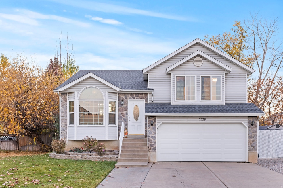 Tri-level home with stone siding, a shingled roof, and a garage