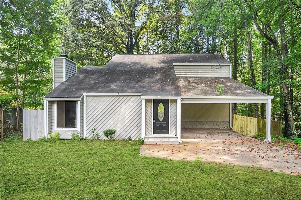 View of front of property featuring view of scattered trees, a carport, a chimney, and driveway