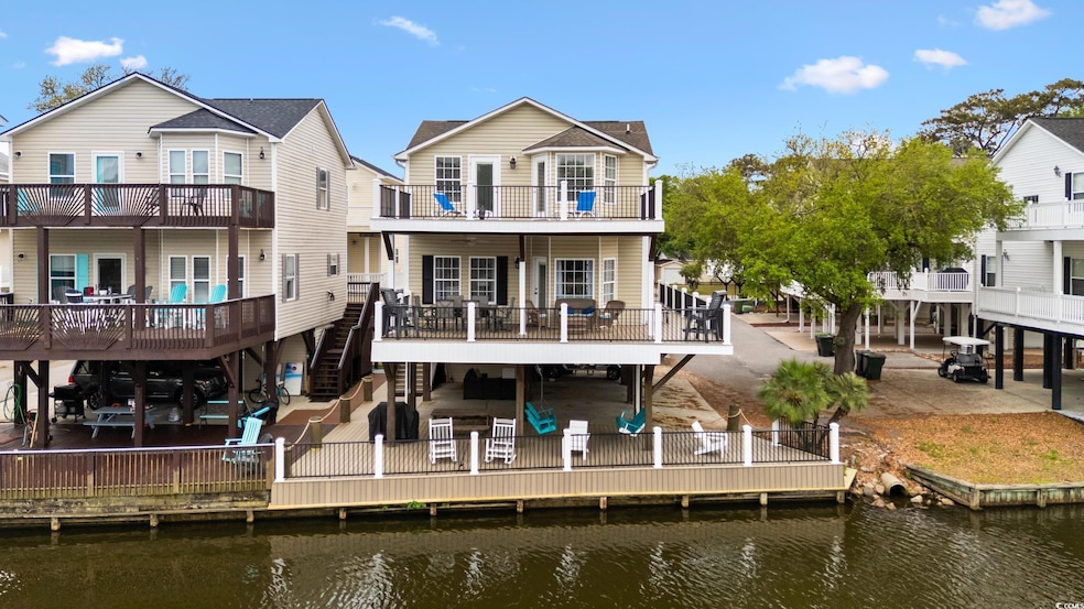 Back of property featuring a deck with water view, stairs, a patio, and a balcony