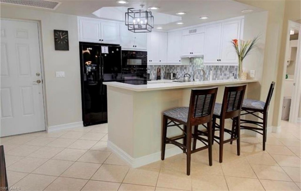 Kitchen with black appliances, a peninsula, a kitchen bar, light tile patterned flooring, and white cabinets
