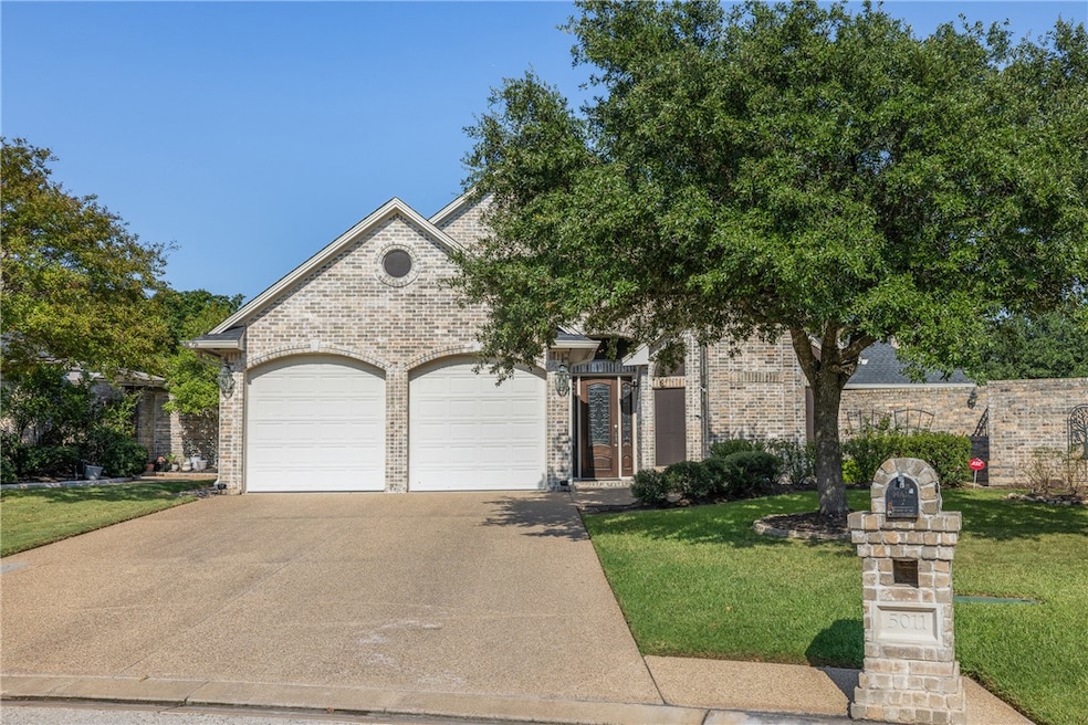 View of front facade featuring driveway, brick siding, a front lawn, and an attached garage