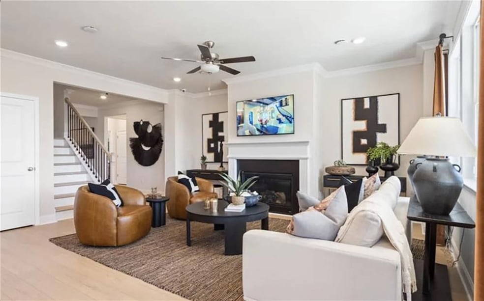 Living area featuring crown molding, stairs, wood finished floors, and a glass covered fireplace